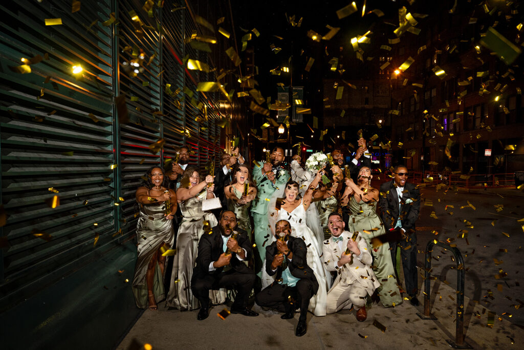 Bridal party and newlyweds celebrating with gold confetti outside the Harold Washington Library in downtown Chicago at the end of the wedding night.