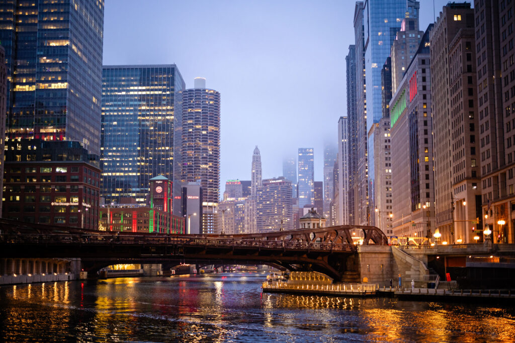 Chicago River skyline at dusk with illuminated bridges and city lights reflecting on the water.