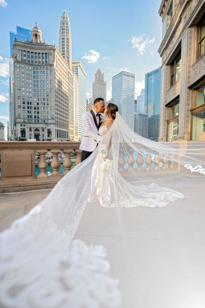 Bride and groom sharing a kiss during downtown Chicago wedding portraits, with flowing veil and city skyline in the background.