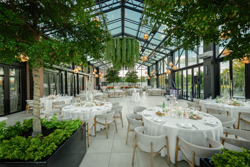 Glass-wrapped wedding reception venue at Pella Signature in Burr Ridge, featuring floor-to-ceiling windows, greenery, and elegant table settings.