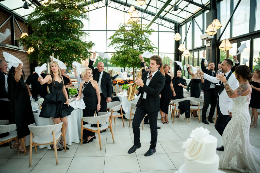 Black-tie wedding reception at Pella Signature in Chicago, with all-black dressed guests celebrating to live saxophone music.